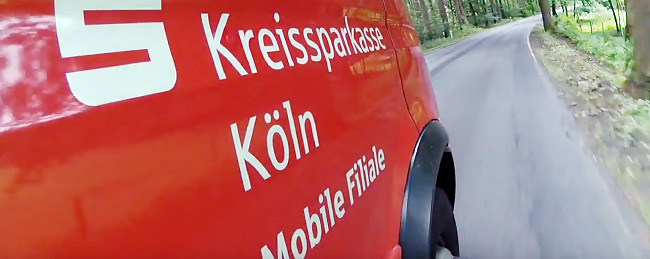 Bewegtbild von einem roten Bus mit der Aufschrift "Kreissparkasse Köln Mobile Filiale" aus einem Video.